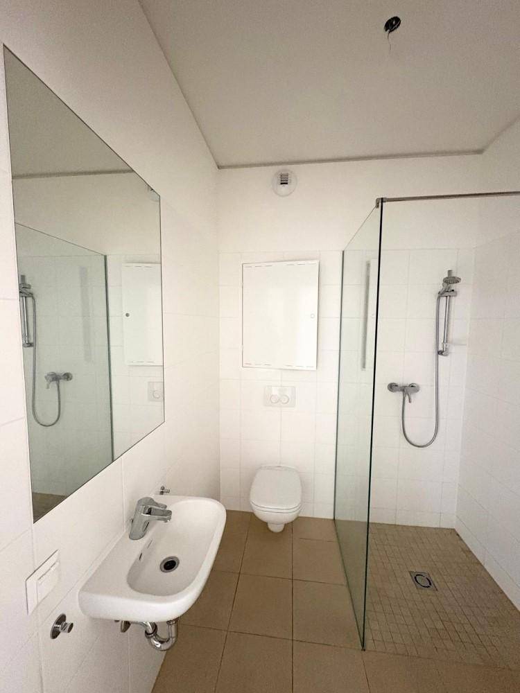 Modernes Badezimmer mit ebenerdiger Dusche, weißen Fliesen und einem einzelnen Waschbecken.