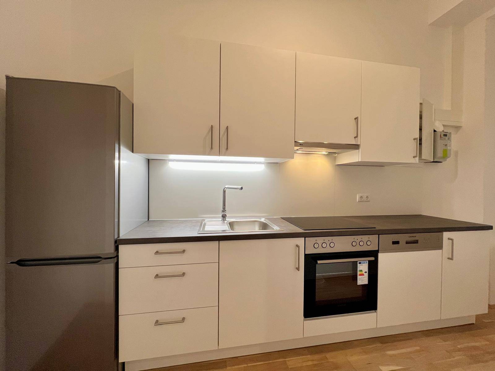 Moderne Einbauküche mit weißen Schränken, integrierten Geräten und Holzboden.