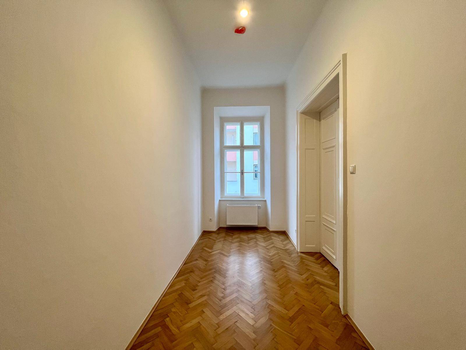 Heller Flur mit Fischgrätparkett und einem Fenster, das Tageslicht spendet.