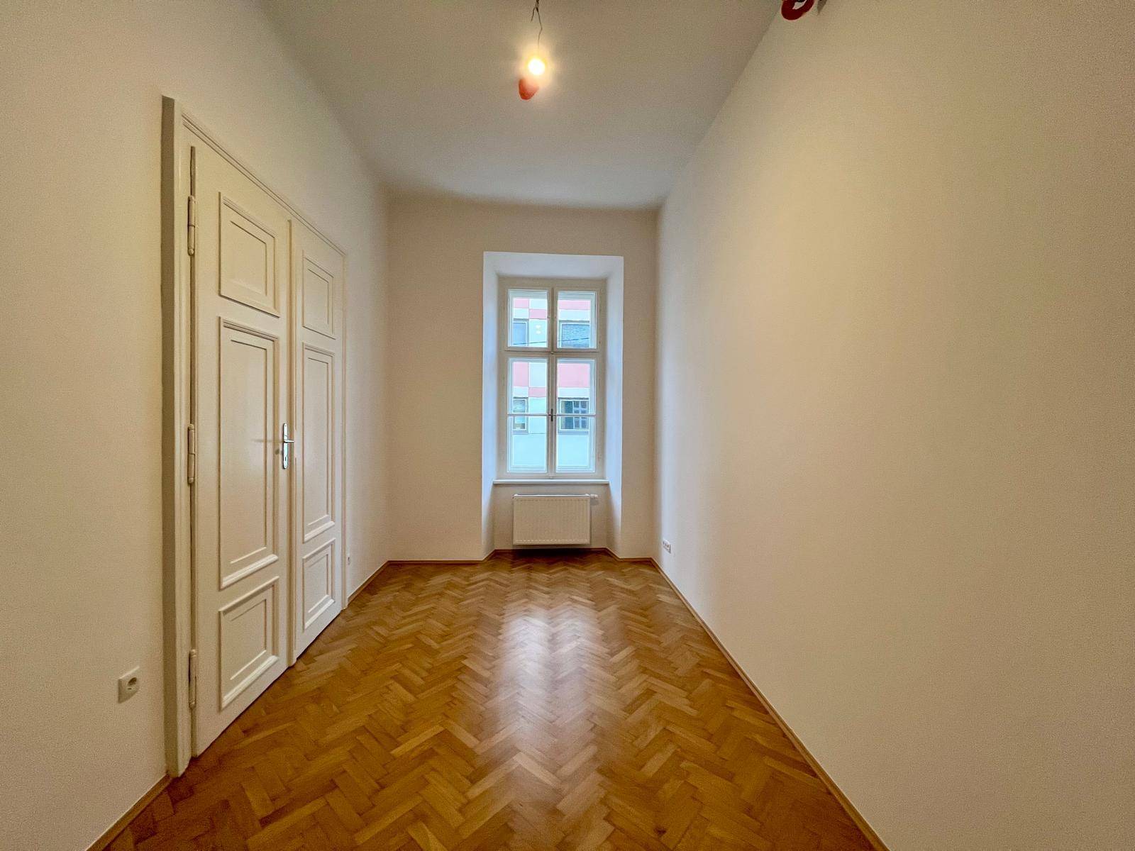 Geräumiges Zimmer mit Fischgrätparkett, Einbauschränken und einem Fenster.