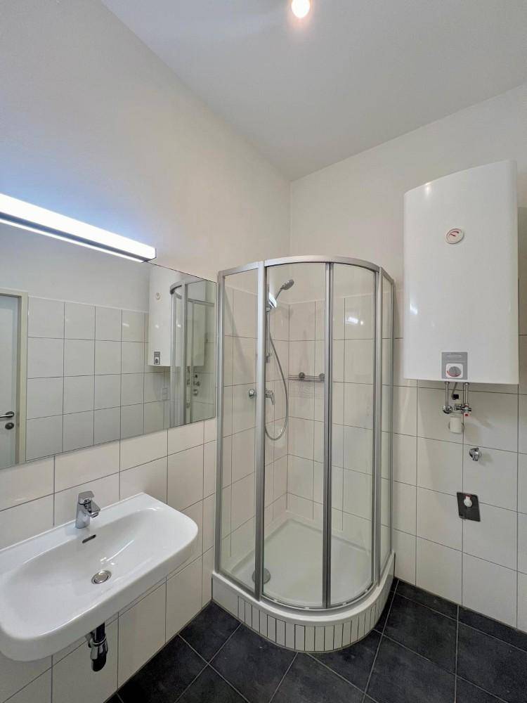 Funktionales Badezimmer mit Duschkabine, Waschbecken und weiß gefliesten Wänden.