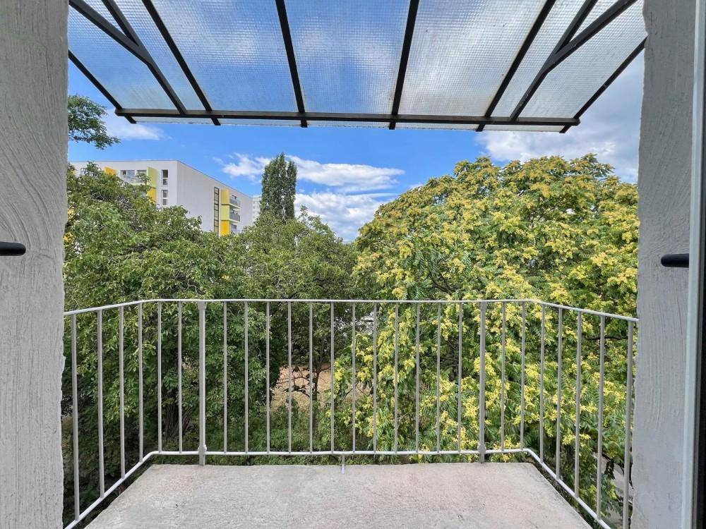 Überdachter Balkon mit Metallgeländer und Blick ins Grüne sowie auf die Wohnbebauung.