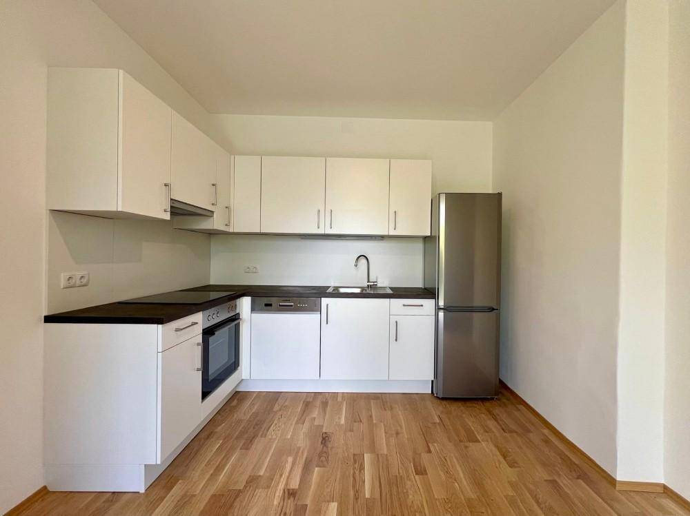 Moderne Einbauküche mit weißen Schränken, dunkler Arbeitsplatte, Geräten und Holzfußboden.
