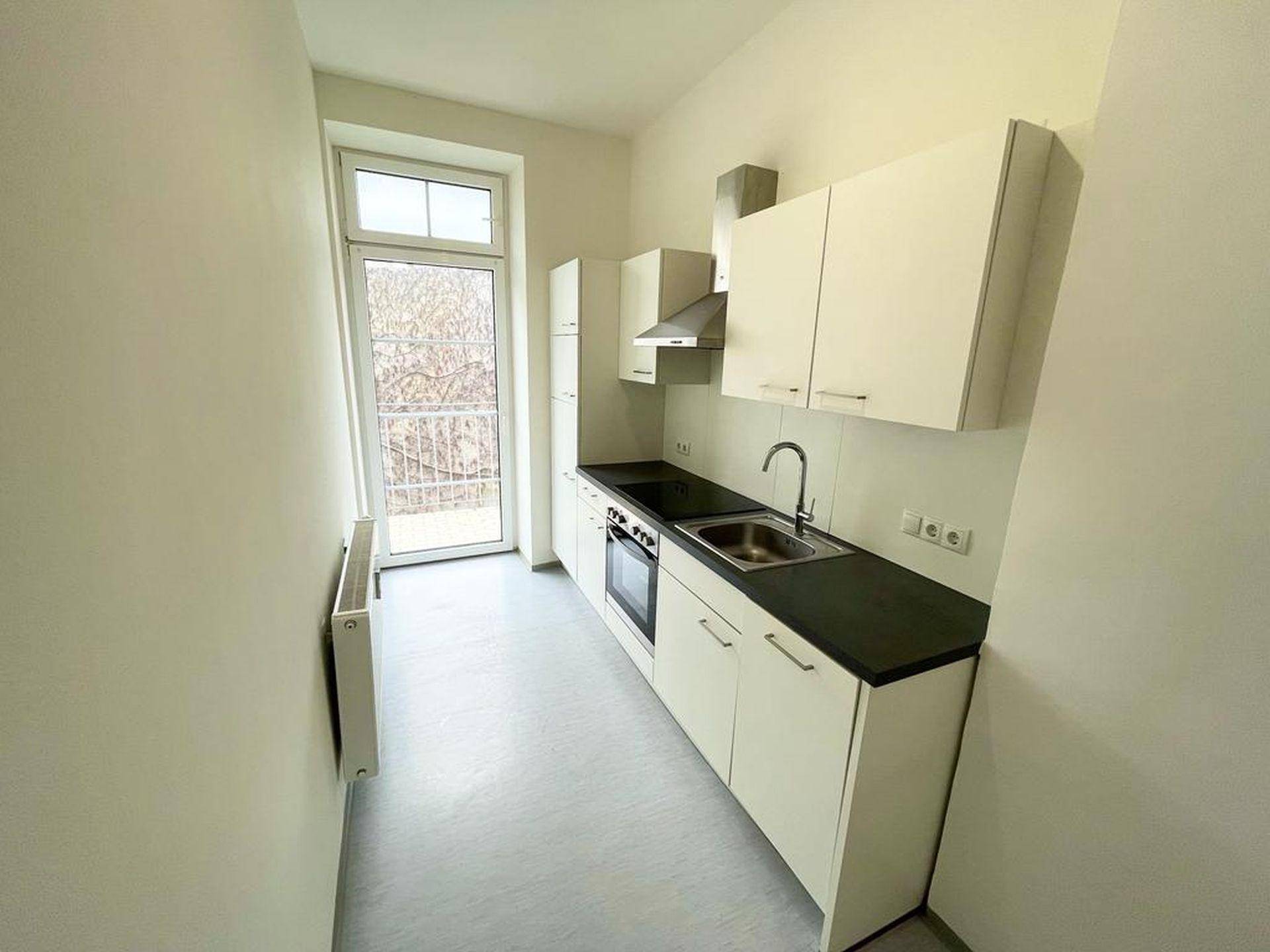 Funktionale Küchenzeile mit weißen Schränken, dunkler Arbeitsplatte und Zugang zum Balkon.