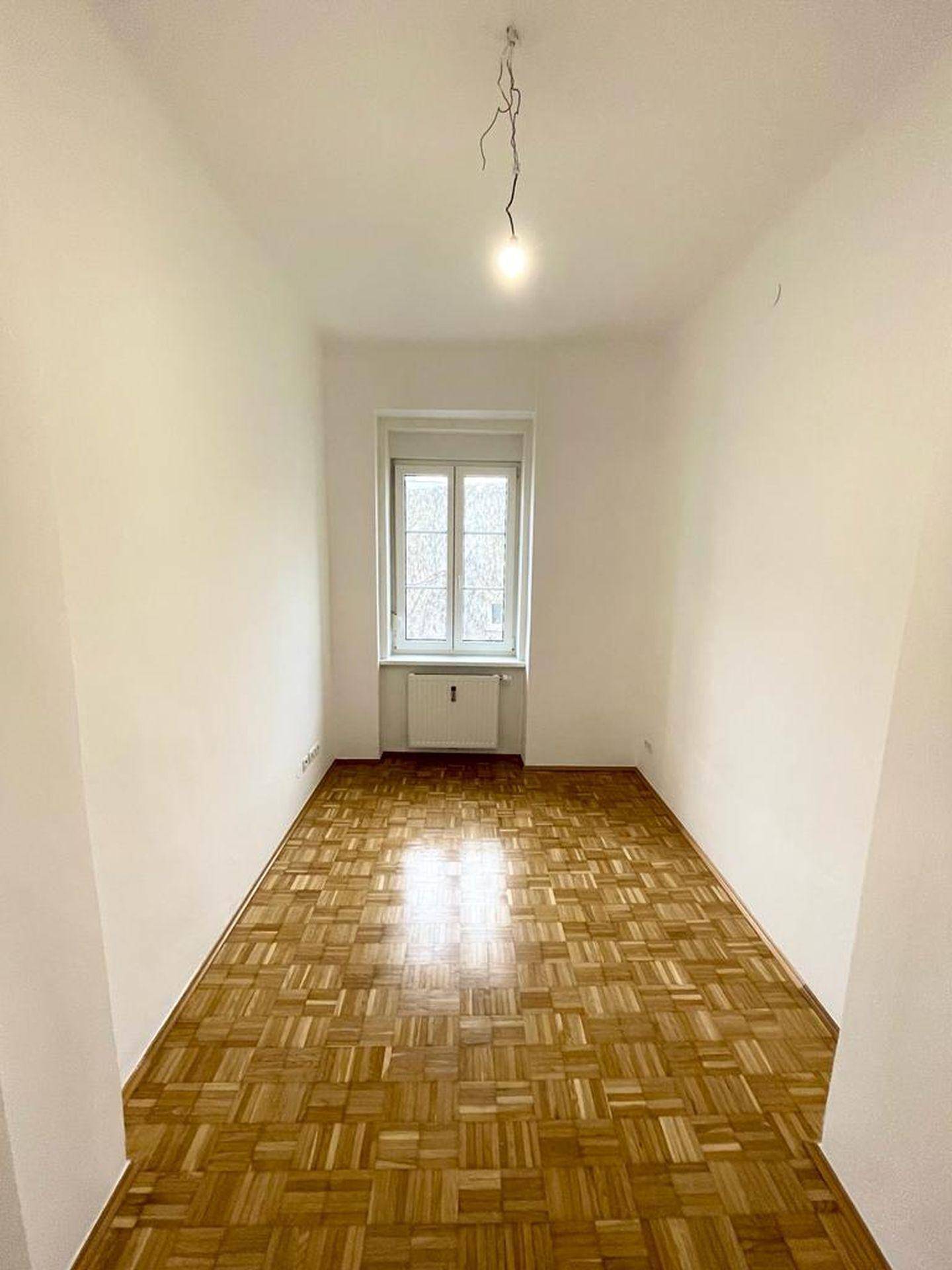Helles, längliches Zimmer mit Parkettboden und einem Fenster, geeignet als Schlaf- oder Arbeitszimmer.