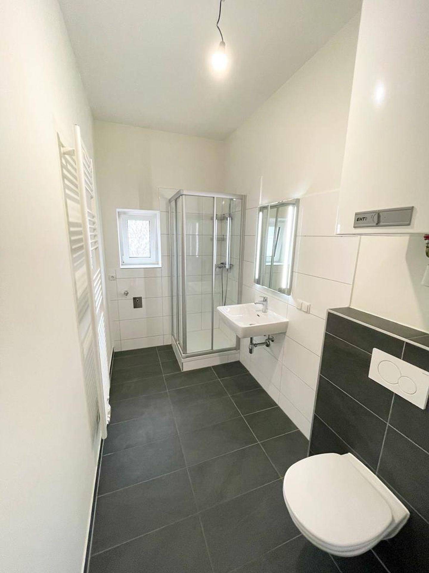 Modernes Badezimmer mit dunklen Bodenfliesen, Duschkabine, Waschbecken und WC.