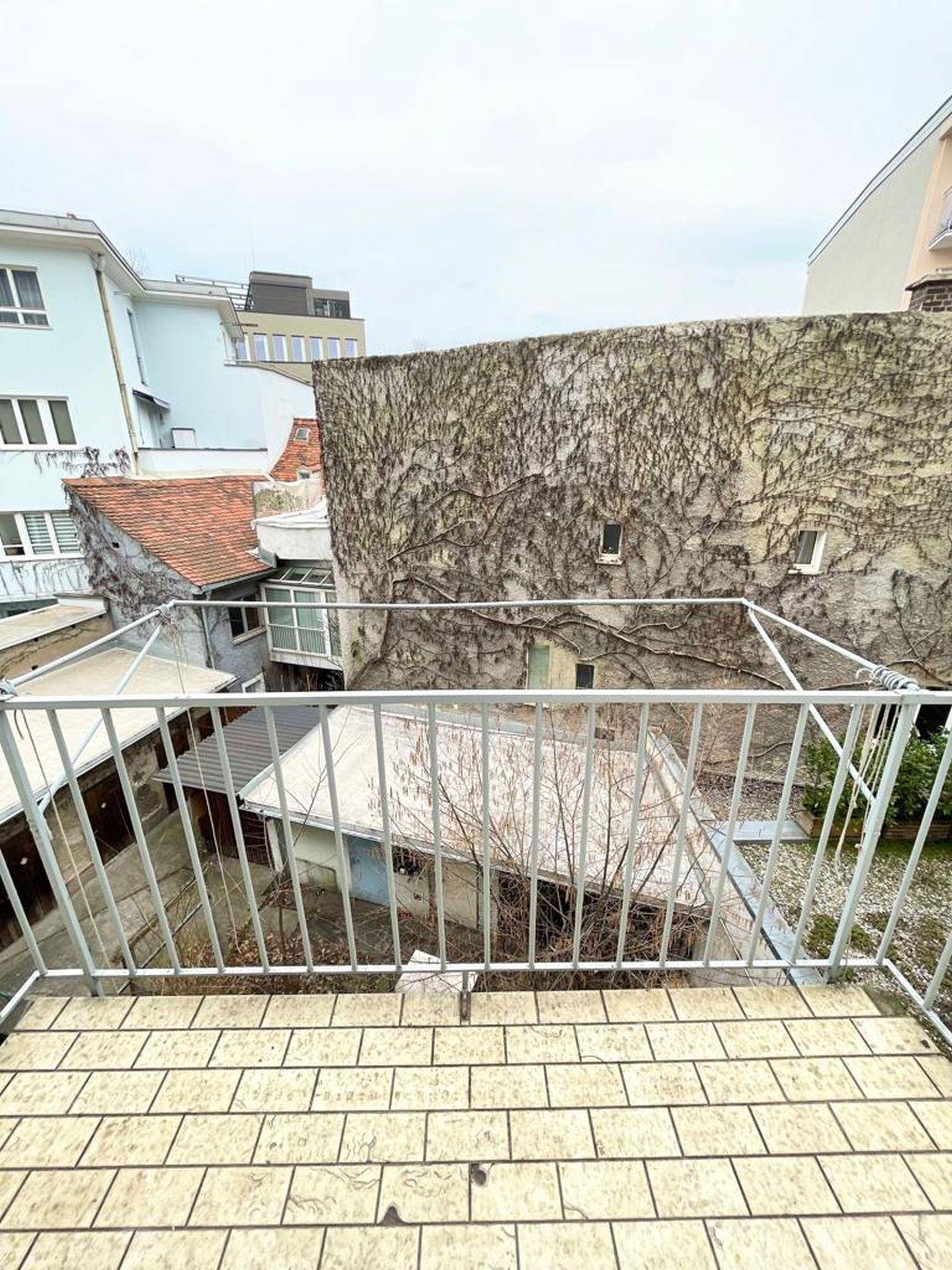 Balkon mit Blick auf einen begrünten Innenhof und umliegende Gebäude.