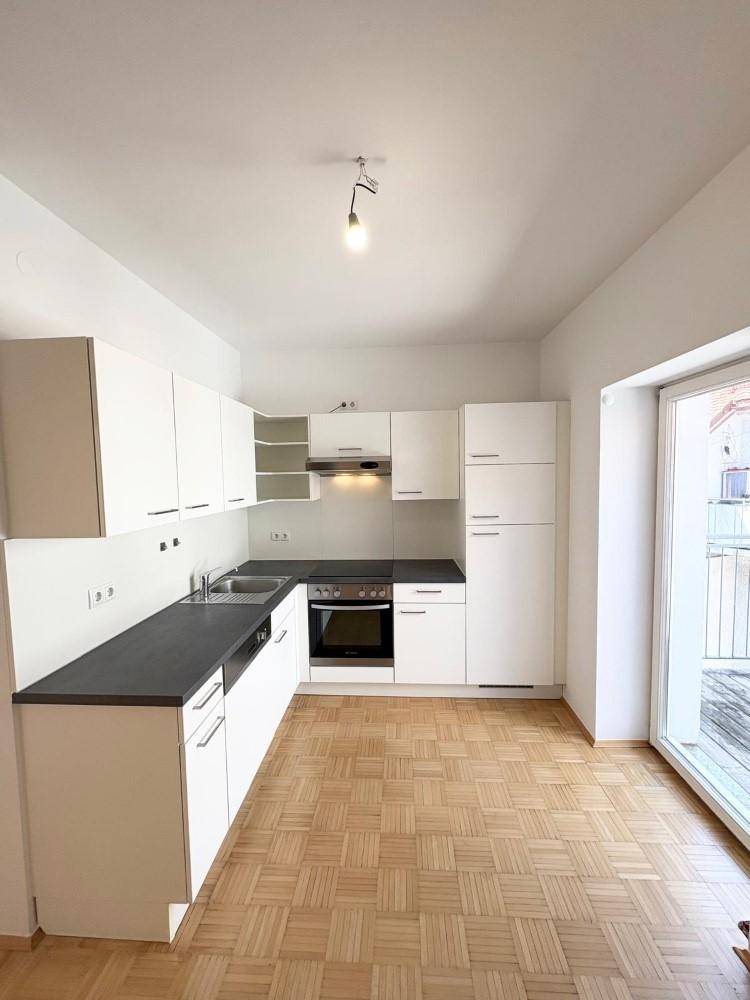 Helle Küche mit weißen Schränken, Parkettboden und direktem Zugang zu einem Balkon.