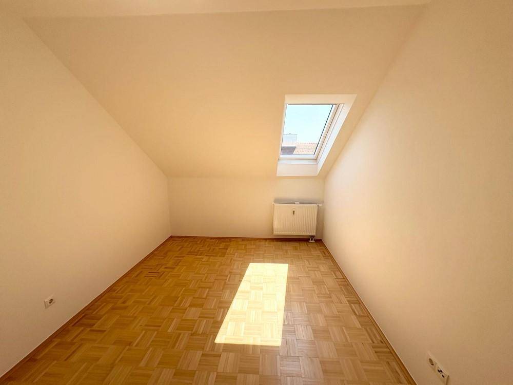Gemütliches Dachzimmer mit Parkettboden und einem Dachfenster, das viel Licht spendet.