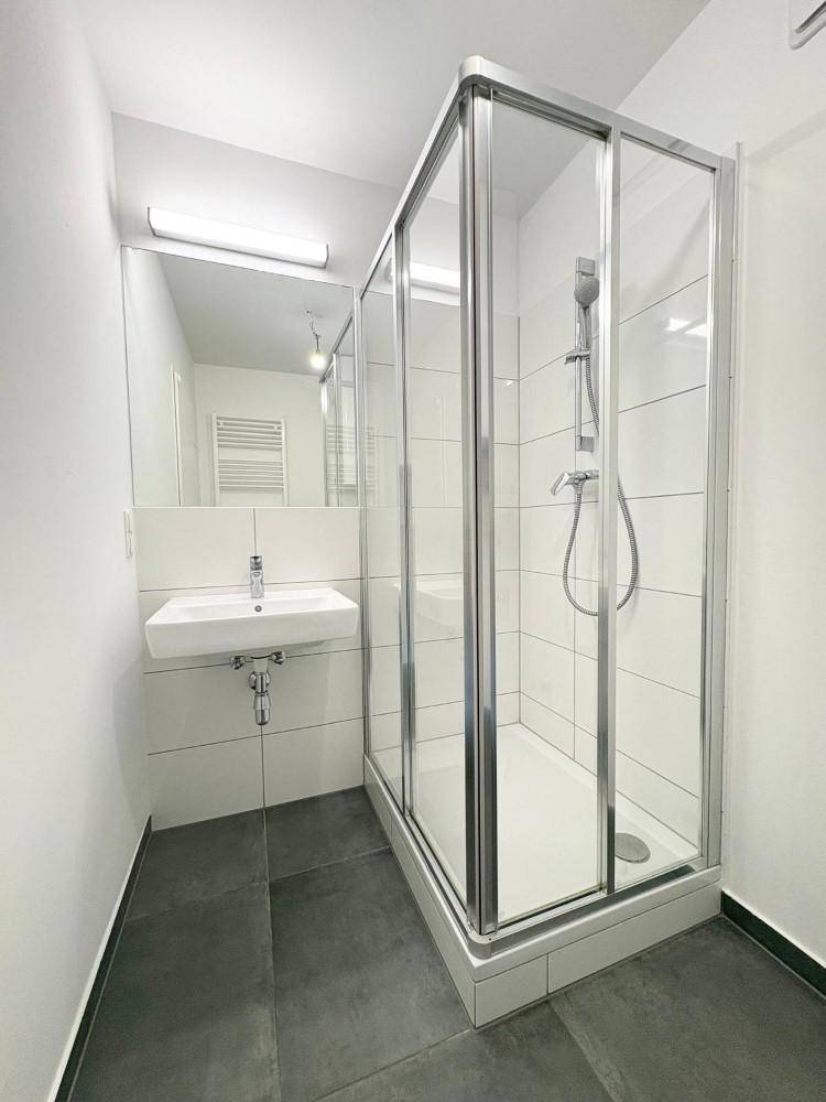 Modernes Badezimmer mit Duschkabine, Waschbecken und dunklen Bodenfliesen.