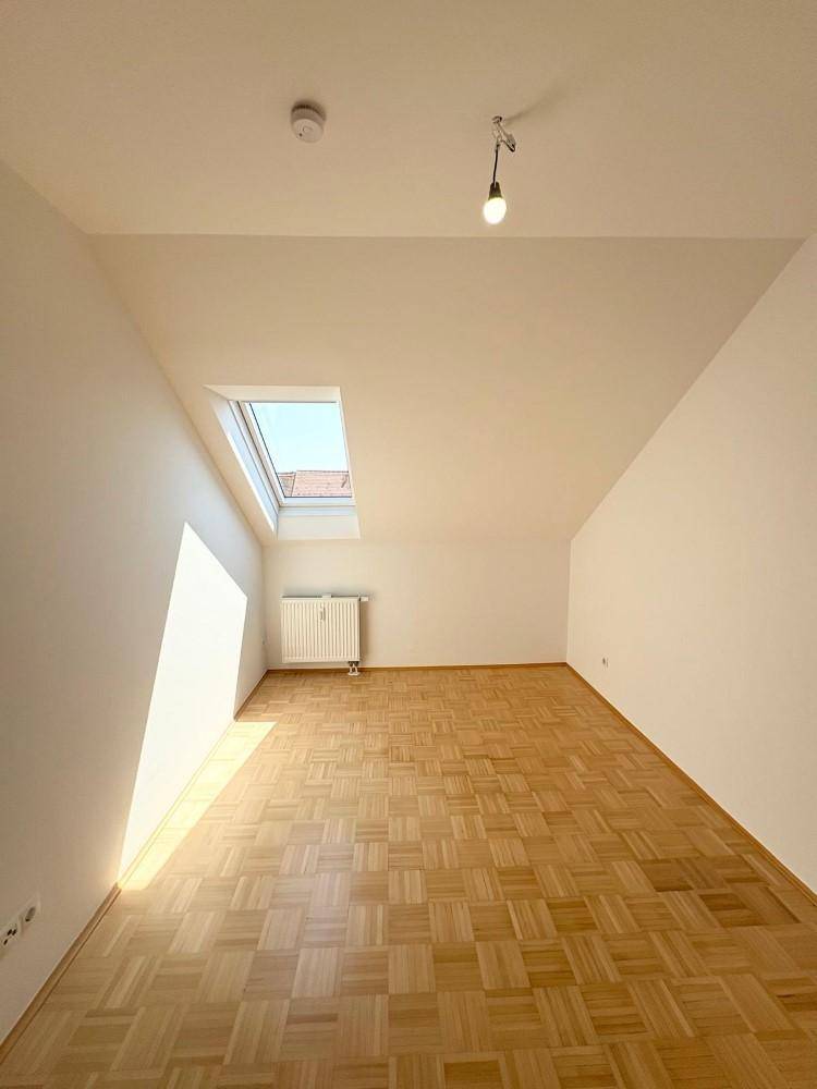 Heller Dachraum mit Parkettboden und schrägen Wänden, durch ein Dachfenster gut belichtet.