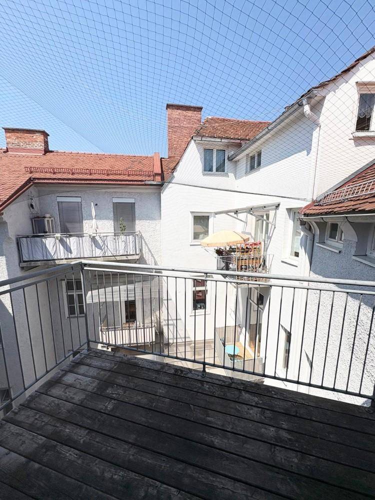 Balkon mit Holzbelag und Metallgeländer, bietet Blick auf den Innenhof des Gebäudes.