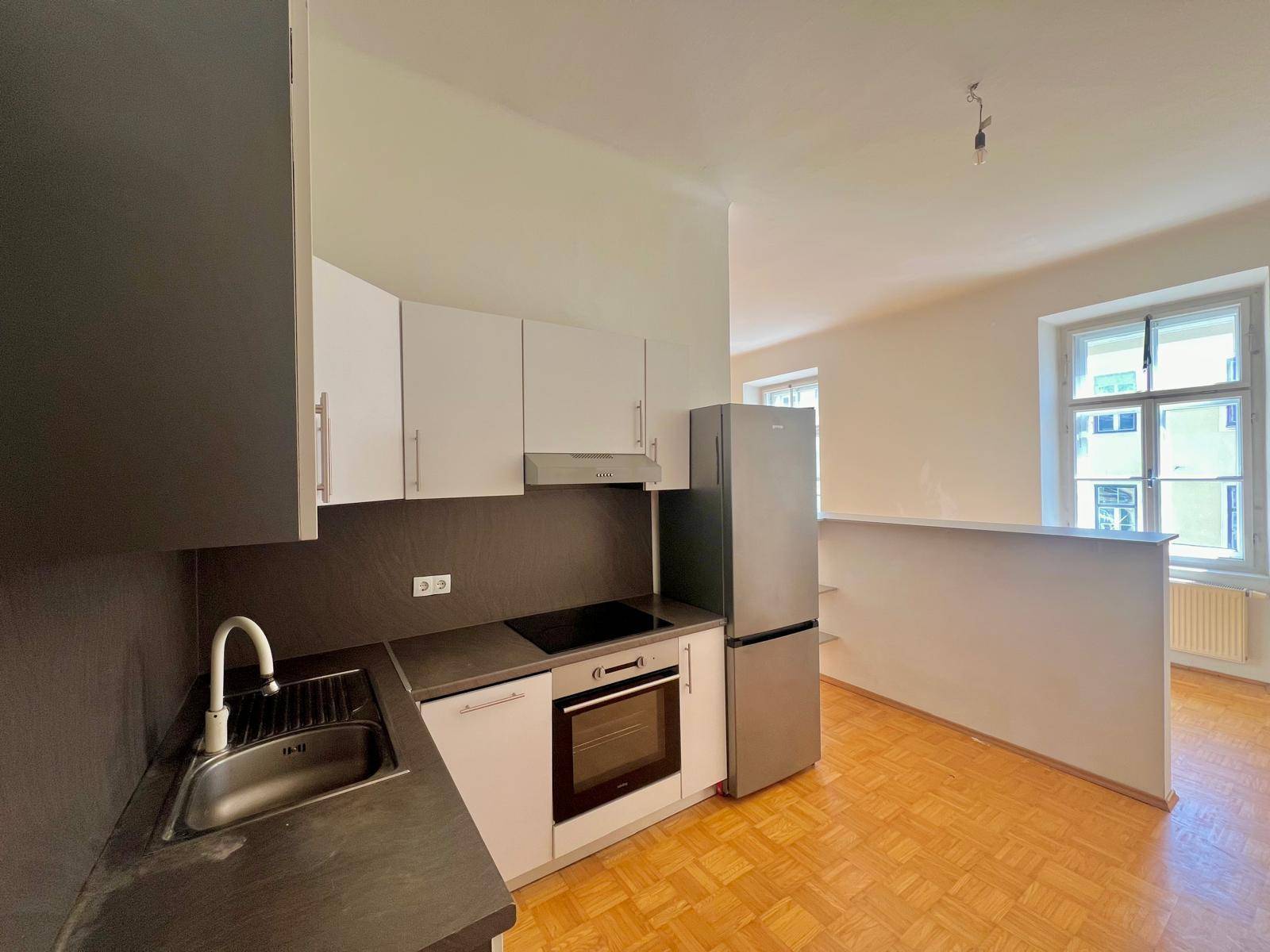 Kompakte Einbauküche mit modernen Geräten und integriertem Kühlschrank in hellem Raum.