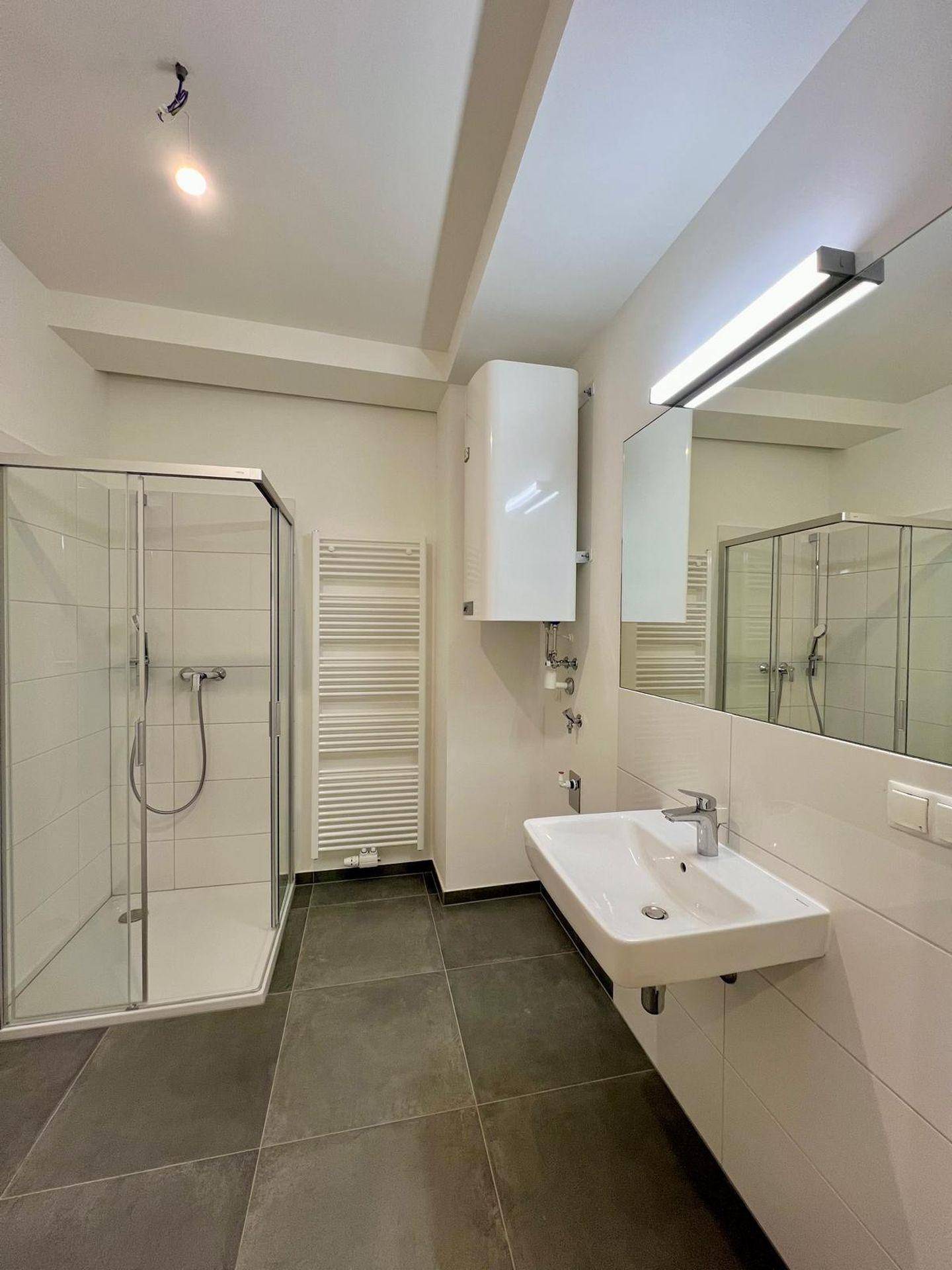 Modernes Badezimmer mit Duschkabine, Waschbecken und beheiztem Handtuchhalter.