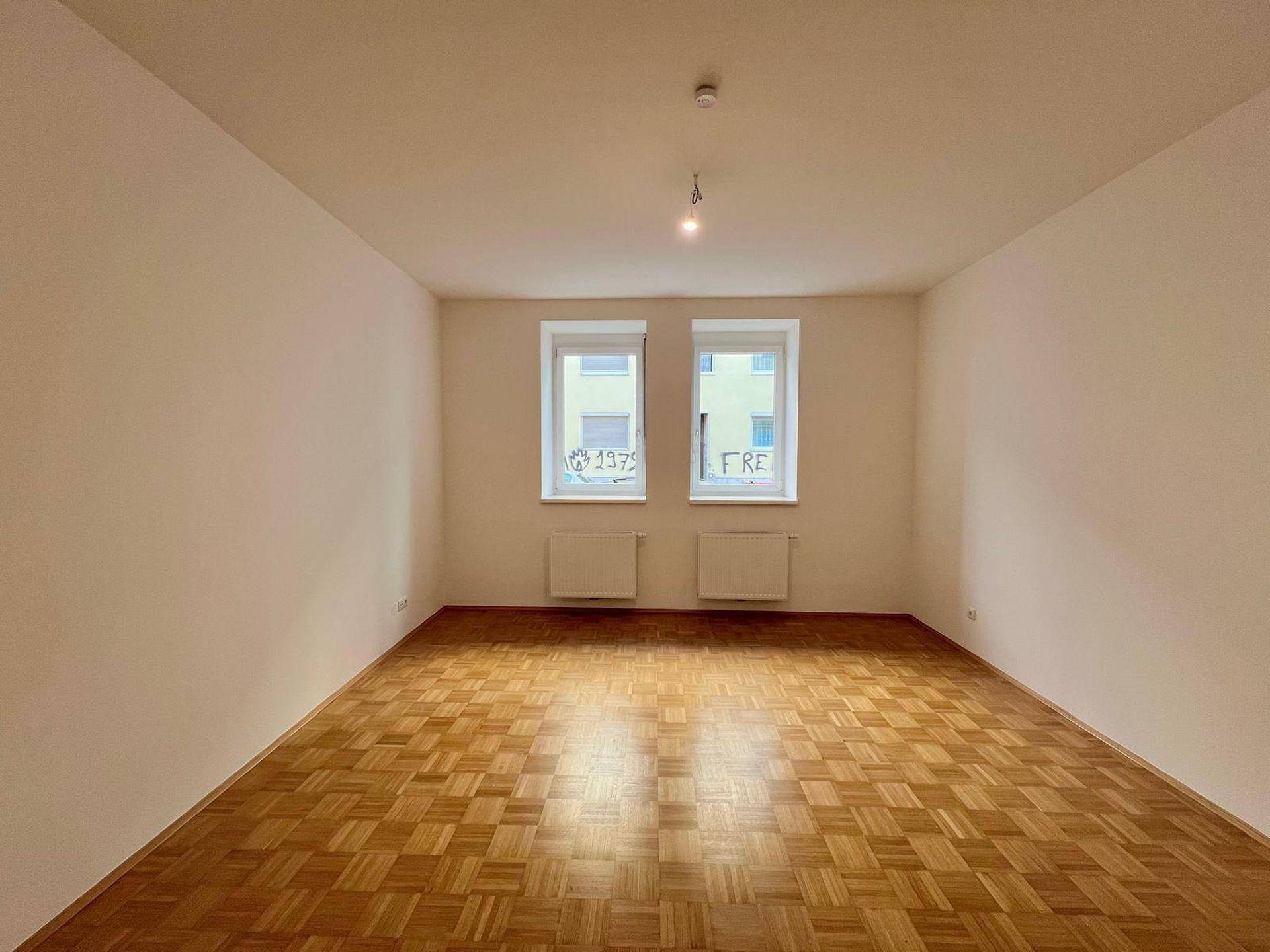 Heller, leerer Raum mit Parkettboden und zwei Fenstern, bereit zum Einzug.