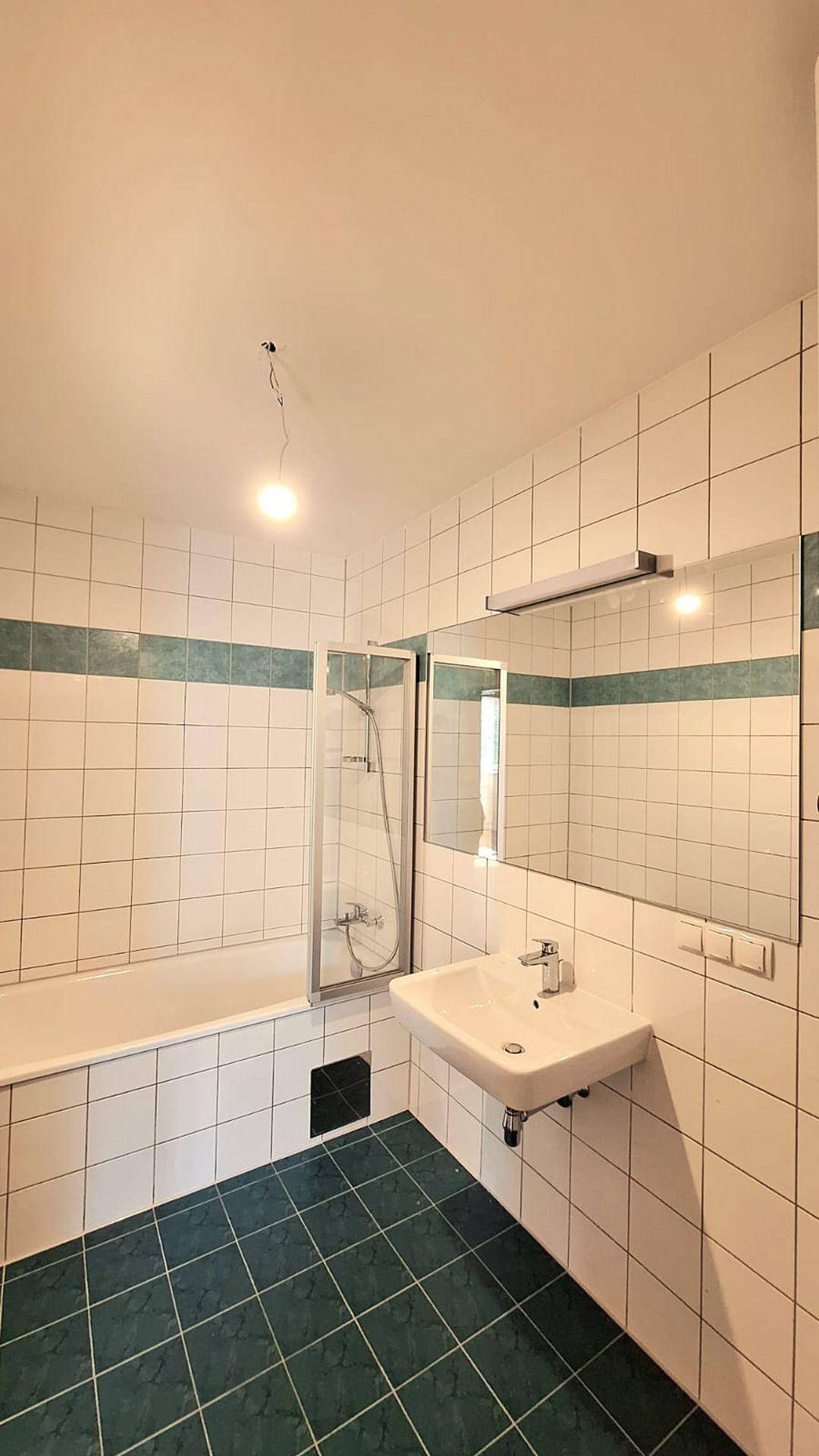 Badezimmer mit Badewanne, Duschabtrennung, Waschbecken und grün-weißen Fliesen.
