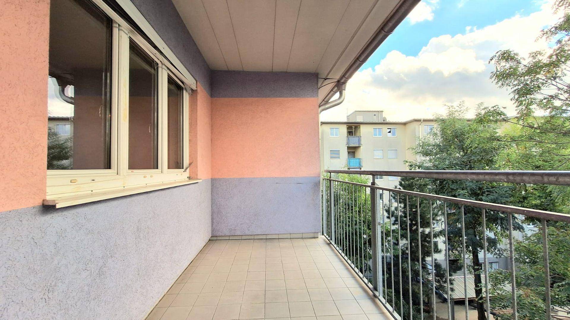 Balkon mit Fliesenboden und Blick ins Grüne sowie auf umliegende Gebäude.