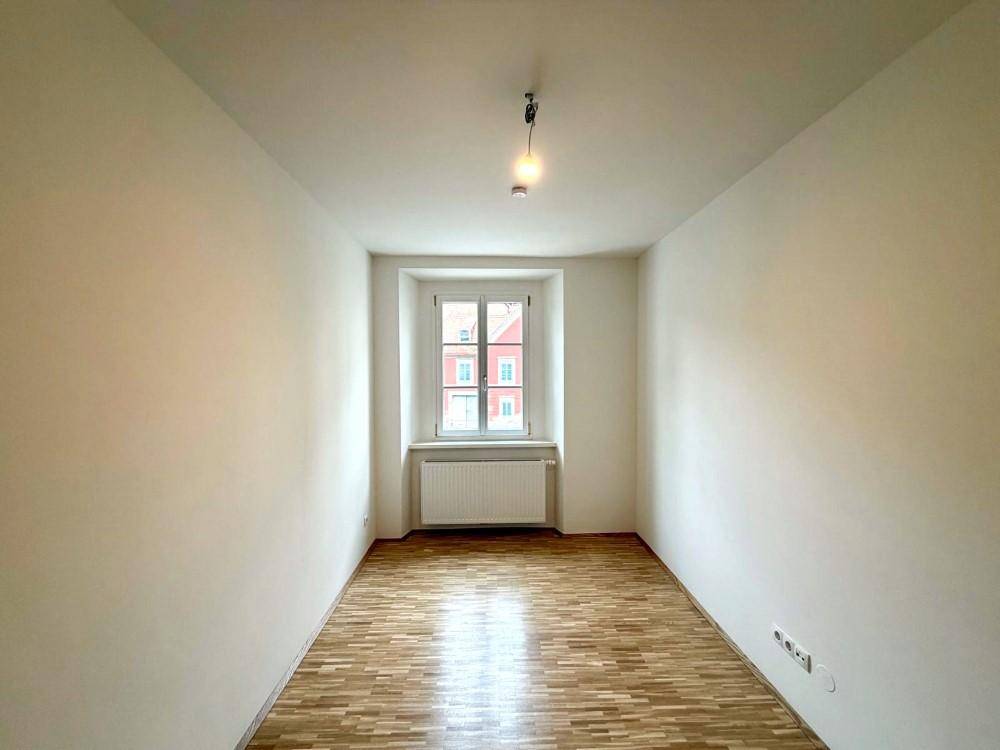 Helles, leeres Zimmer mit Parkettboden und einem Fenster, ideal als Schlaf- oder Arbeitszimmer.