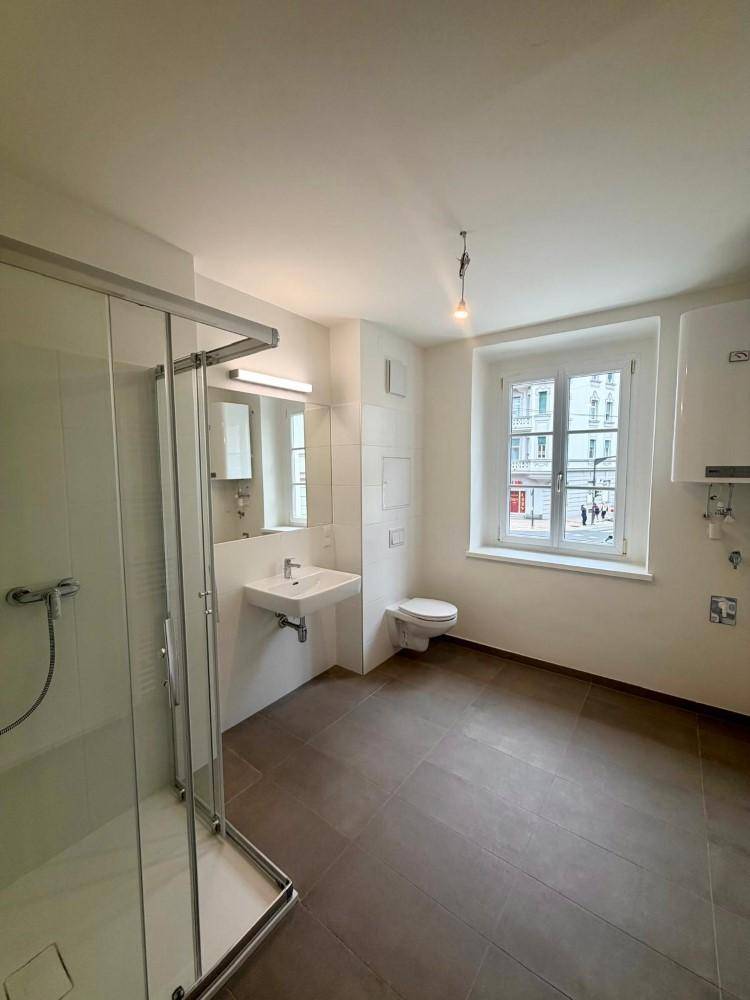 Modernes Badezimmer mit ebenerdiger Dusche, Waschbecken, WC und Fenster für Tageslicht.