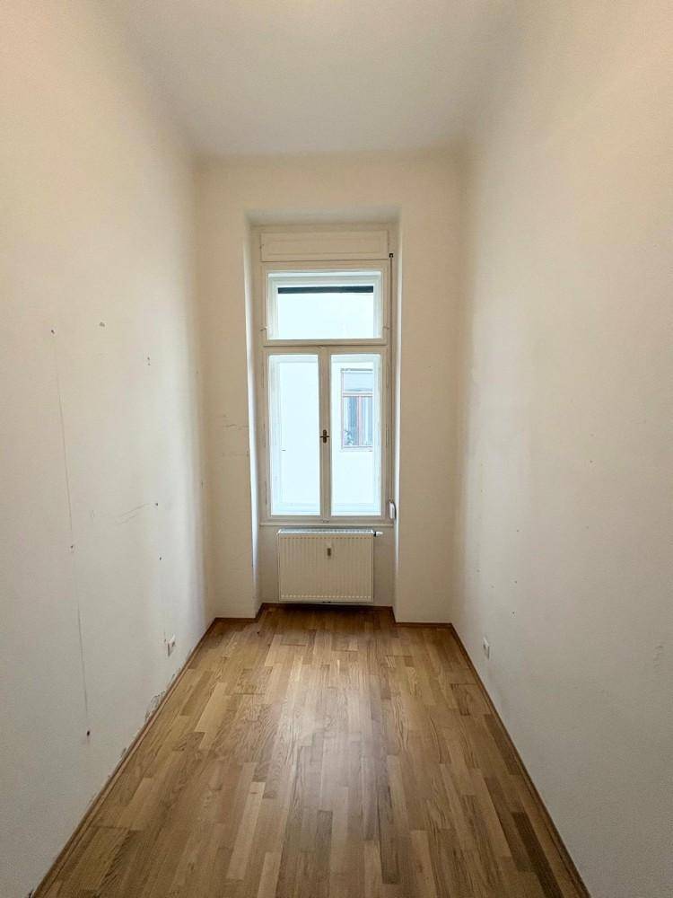 Sehr schmaler Raum mit Laminatboden und Fenster, dessen Nutzung unklar ist.