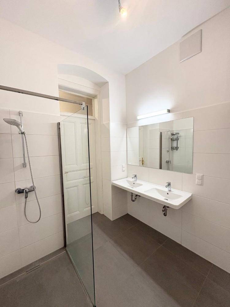 Modernes Badezimmer mit Doppelwaschbecken, großer begehbarer Dusche und hellen Fliesen.