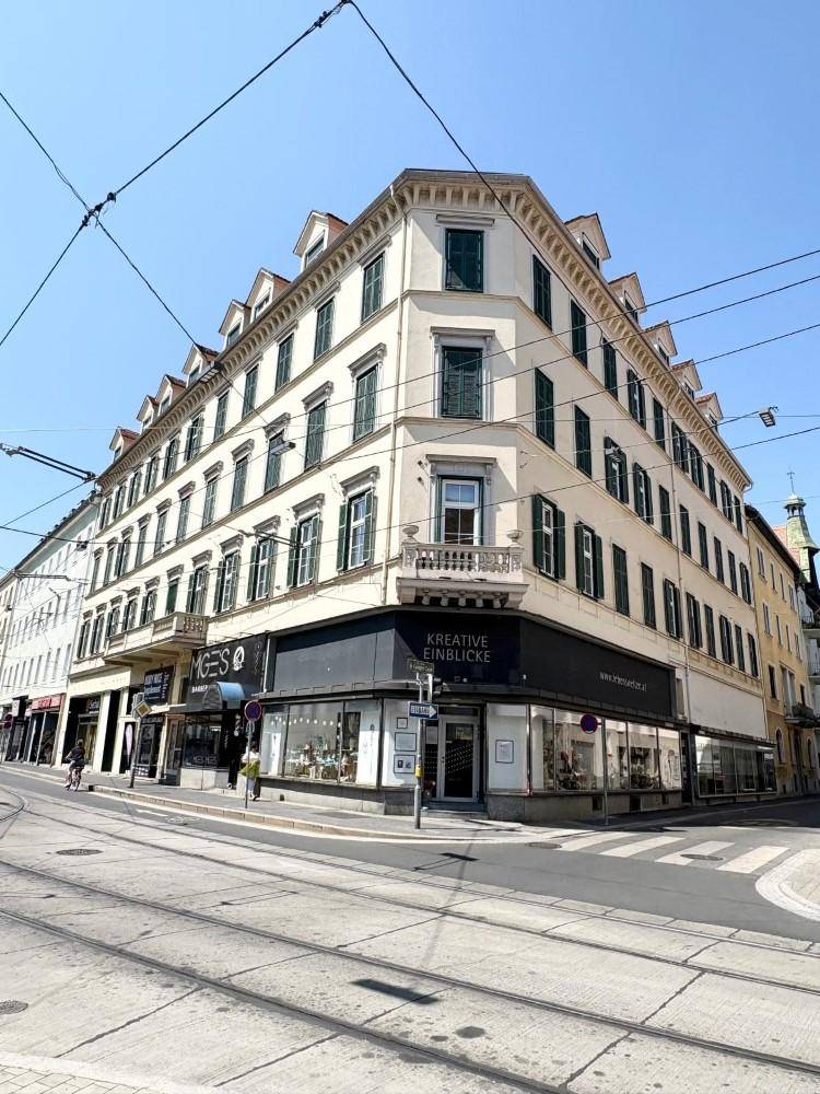 Historisches Eckgebäude mit klassischer Architektur und Geschäften im Erdgeschoss an einer belebten Straße.
