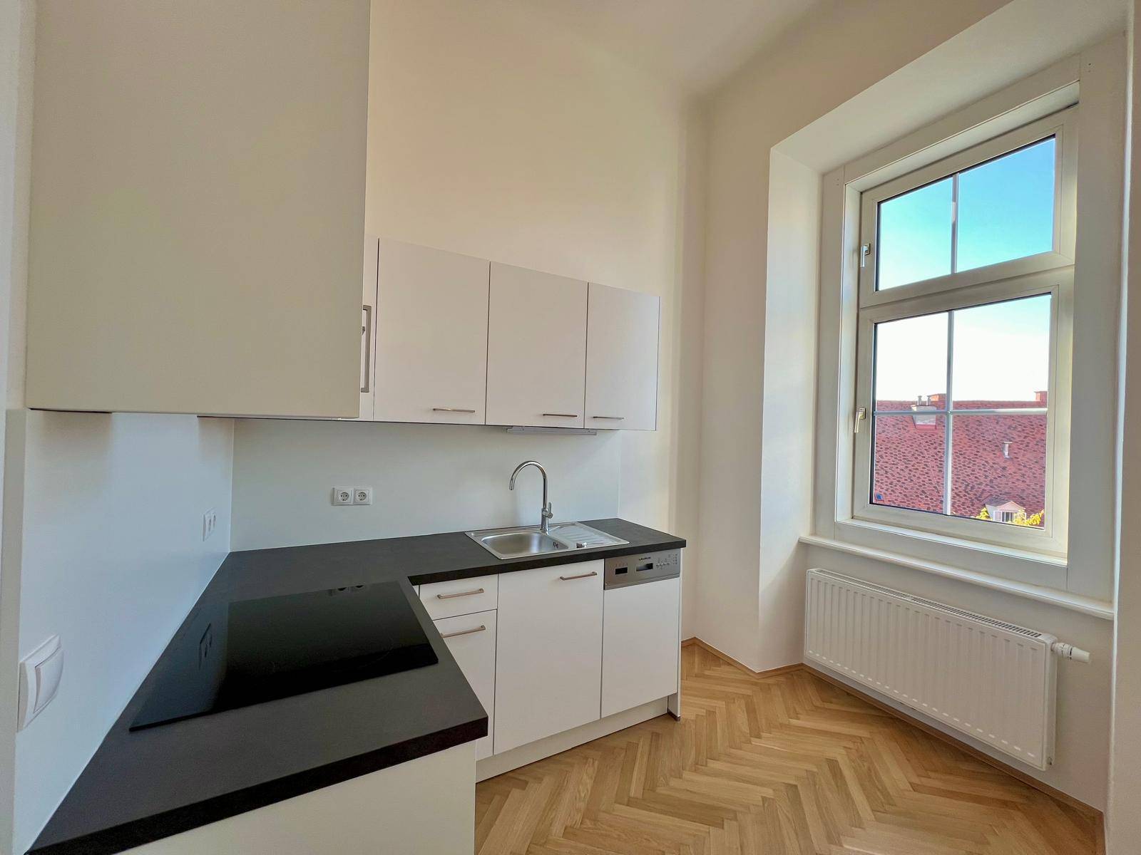 Moderne Küchenzeile mit weißen Schränken, dunkler Arbeitsplatte und Induktionskochfeld.