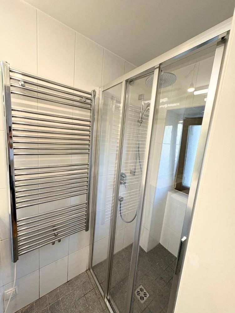 Modernes Badezimmer mit Duschkabine, weißen Fliesen und einem beheizten Handtuchhalter.