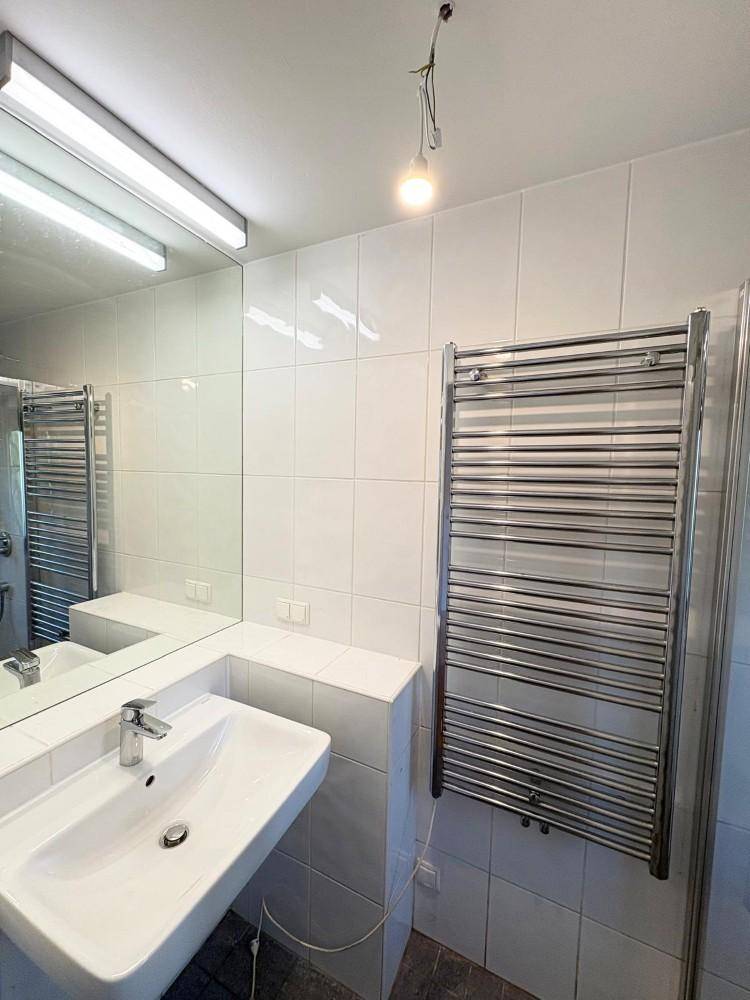 Badezimmer mit Waschbecken, großem Spiegel, weißen Fliesen und beheiztem Handtuchhalter.