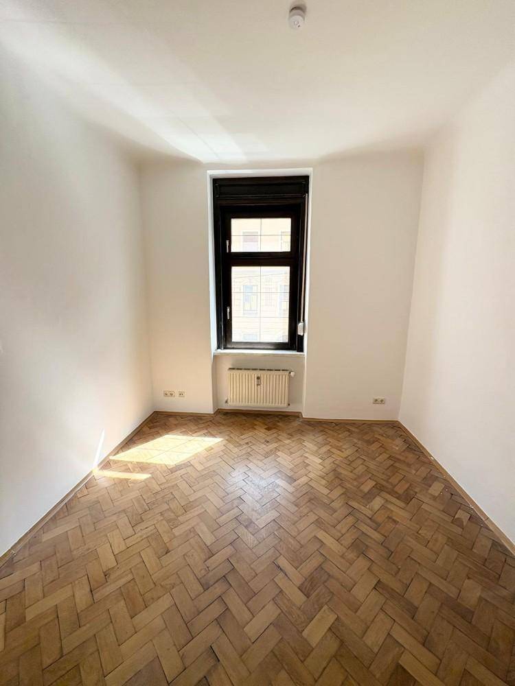 Helles Zimmer mit Fischgrätparkettboden und einem Fenster, das für gute Belichtung sorgt.