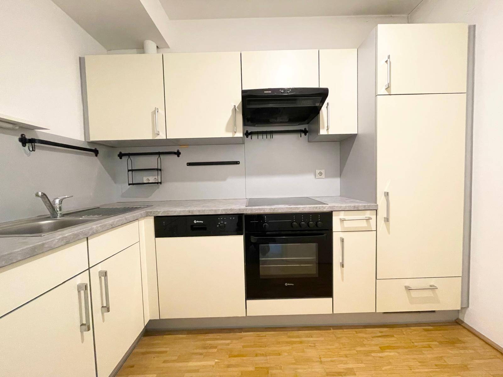 Funktionale Einbauküche in hellem Beige mit integrierten Geräten und Parkettboden.