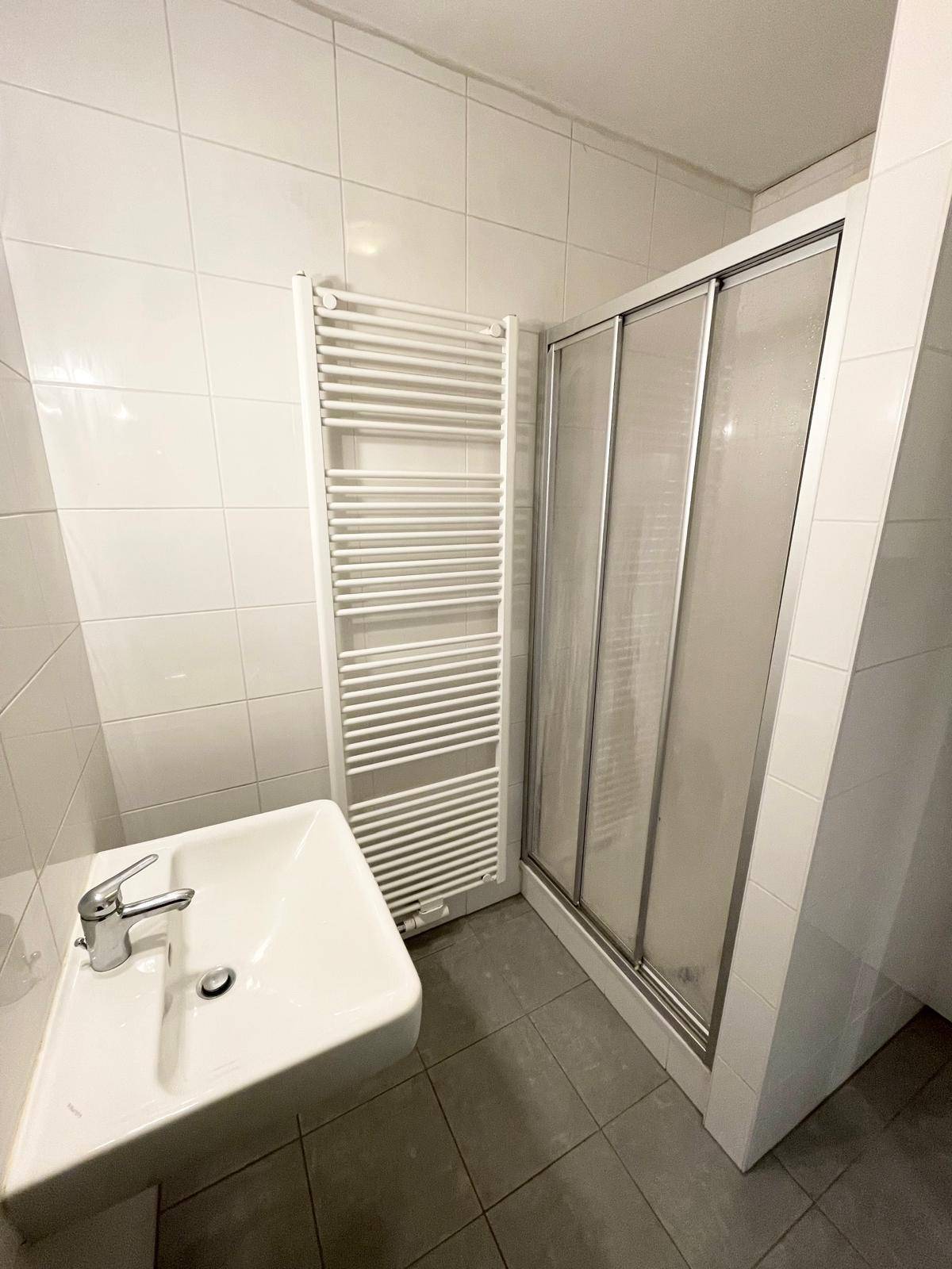 Modernes Badezimmer mit weiß gefliesten Wänden, Dusche und beheiztem Handtuchhalter.