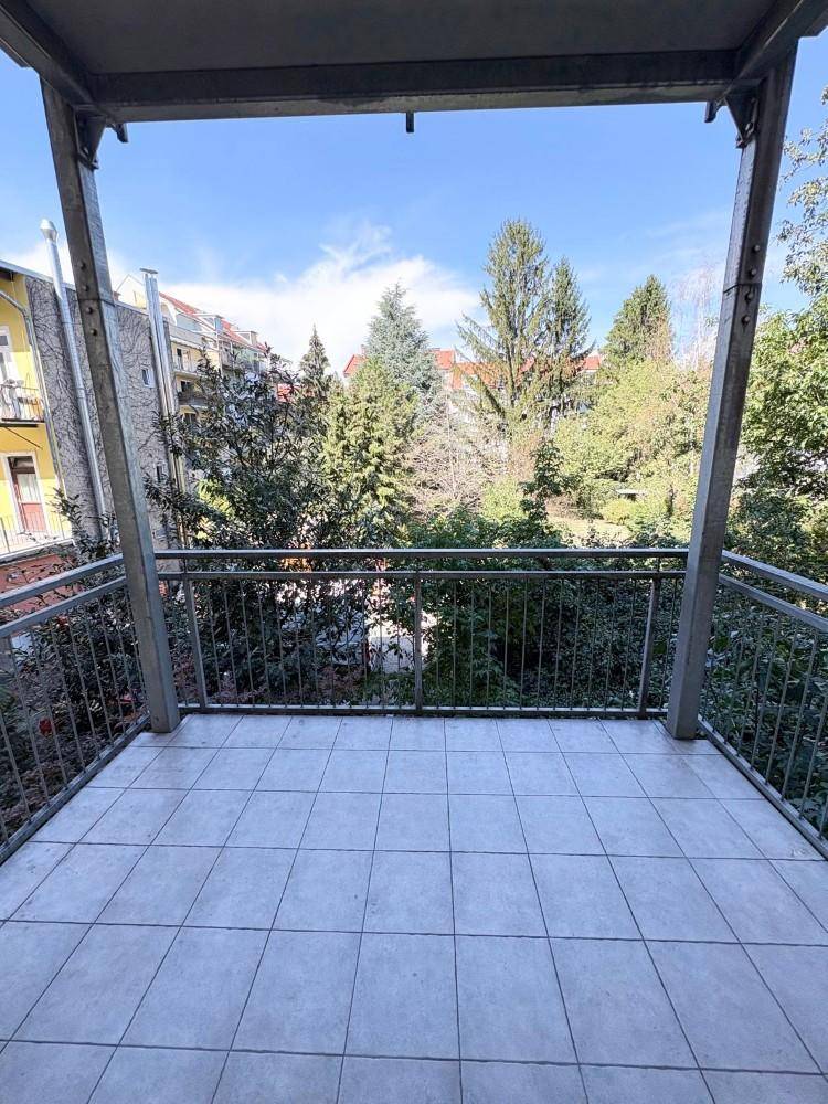 Geräumiger Balkon mit Fliesenboden und Blick ins Grüne sowie auf umliegende Gebäude.