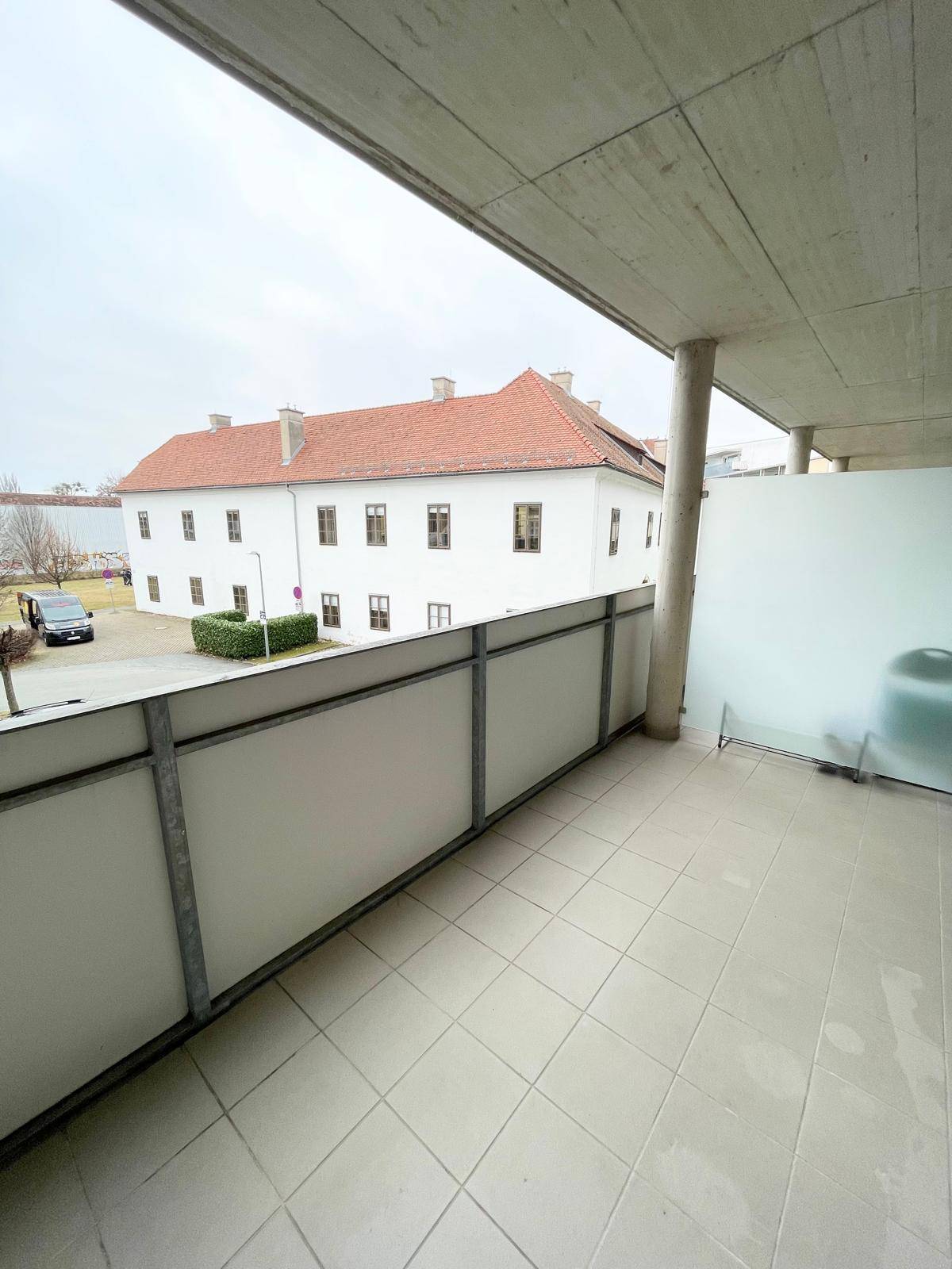 Geräumiger Balkon mit Fliesenboden und Blick auf ein gegenüberliegendes Gebäude.