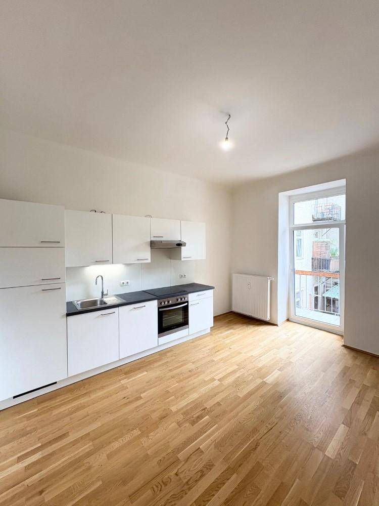 Helle Küche mit weißen Schränken, Holzfußboden und direktem Zugang zu einem Balkon.