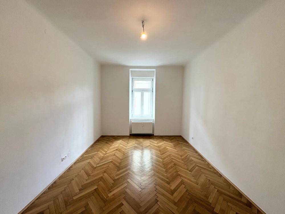 Heller Raum mit klassischem Fischgrätparkett und einem großen Fenster, frisch renoviert.