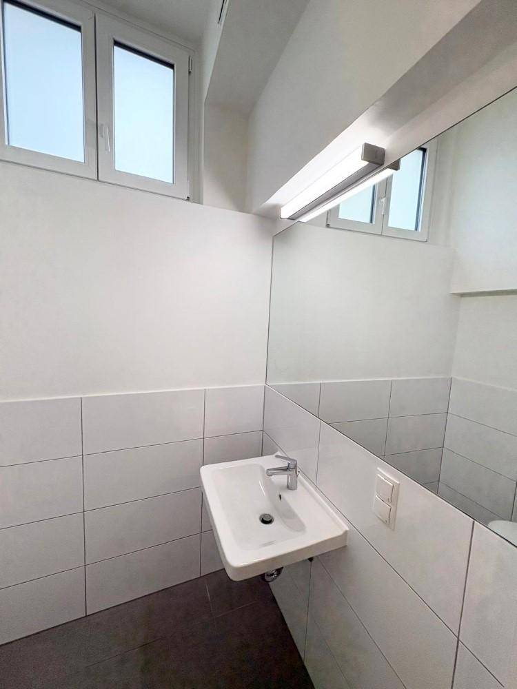 Helles Badezimmer mit modernem Waschbecken, großem Spiegel und Fenster für Tageslicht.