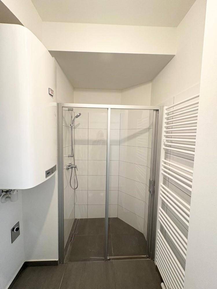 Modernes Badezimmer mit Duschkabine, Fliesenboden, Handtuchheizkörper und Warmwasserboiler.