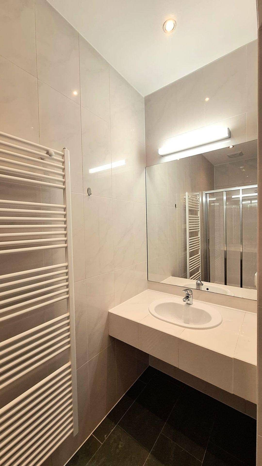 Modernes Badezimmer mit hellen Wandfliesen, dunklem Boden und beheiztem Handtuchhalter.