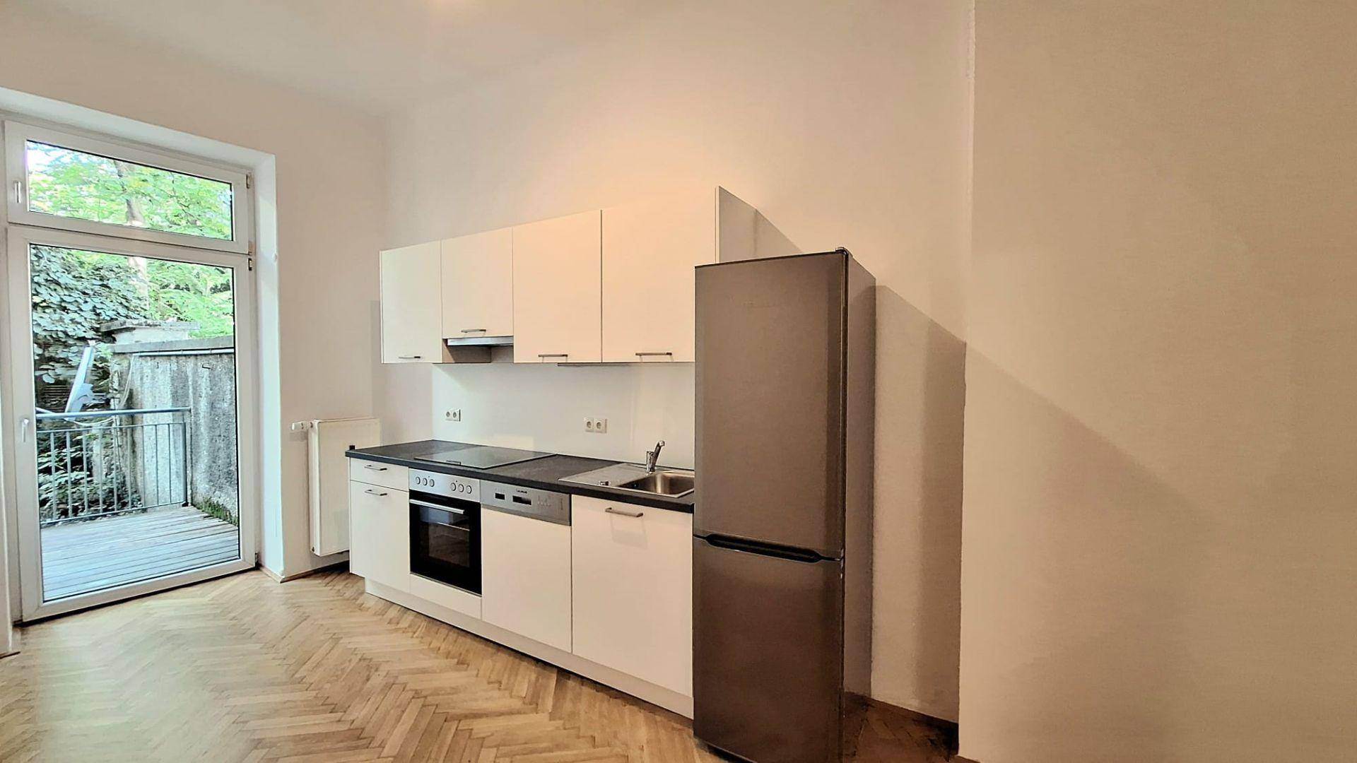 Funktionale Küche mit weißen Schränken, Einbaugeräten und Zugang zu einem Außenbereich.