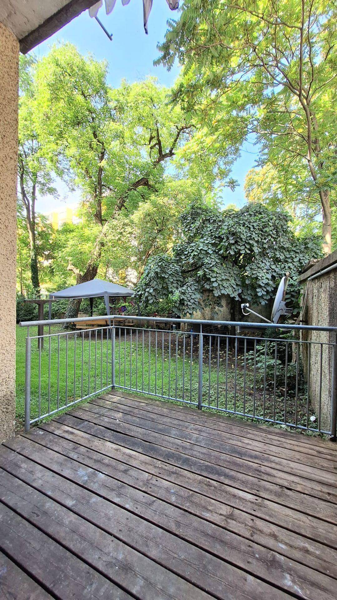 Holzterrasse mit Metallgeländer und Blick auf einen grünen Garten mit alten Bäumen.