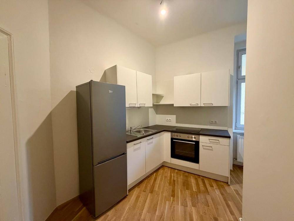 Kleine, funktionale Küche mit weißen Schränken, dunkler Arbeitsplatte und Kühlschrank.