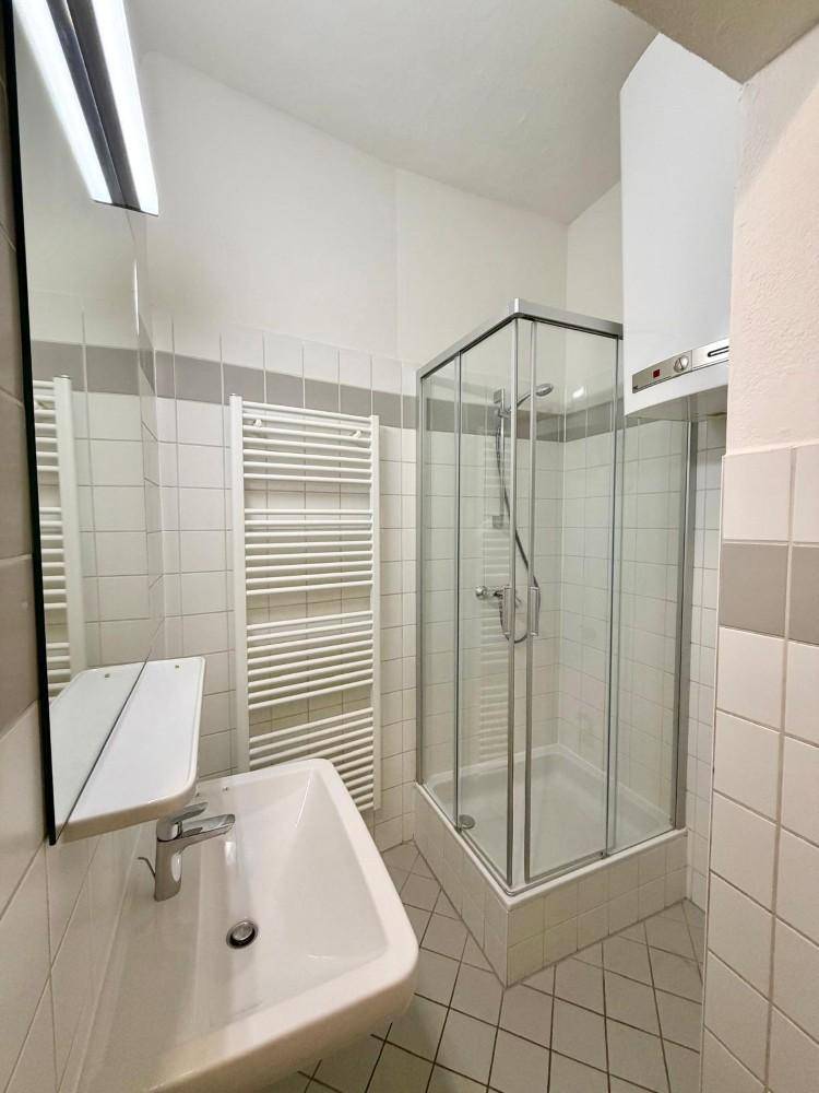 Funktionales Badezimmer mit Duschkabine, Waschbecken, Spiegel und Handtuchheizkörper.