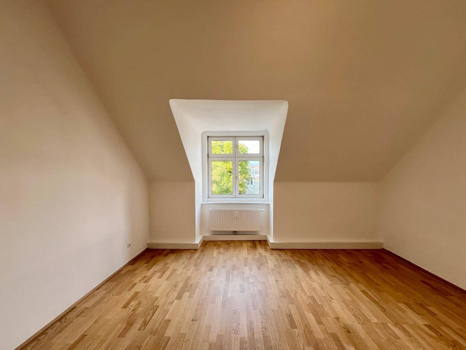 Geräumiges Dachgeschosszimmer mit schrägen Wänden und hellem Holzboden.