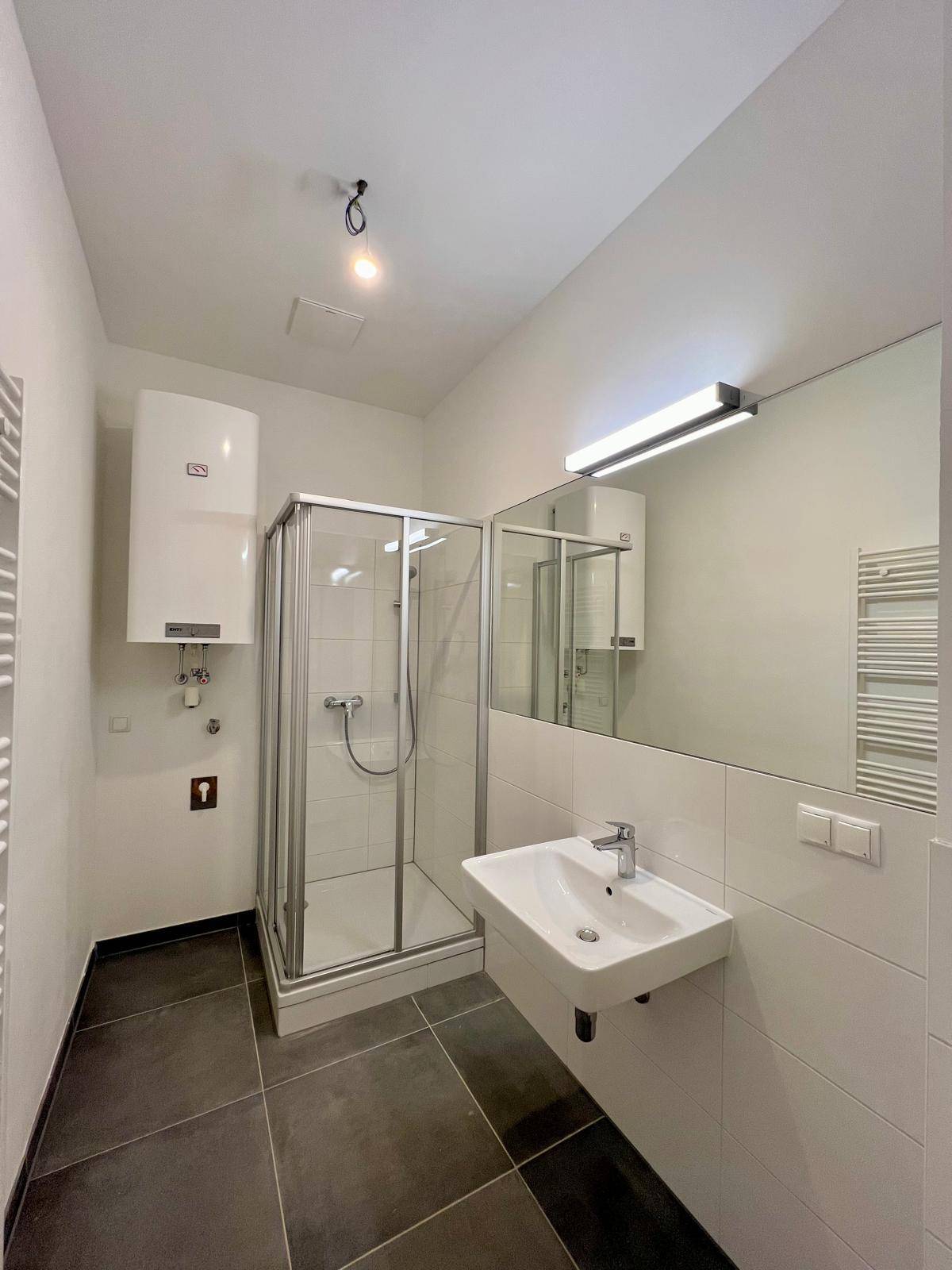 Modernes Badezimmer mit Duschkabine, Einzelwaschbecken und dunklen Bodenfliesen.