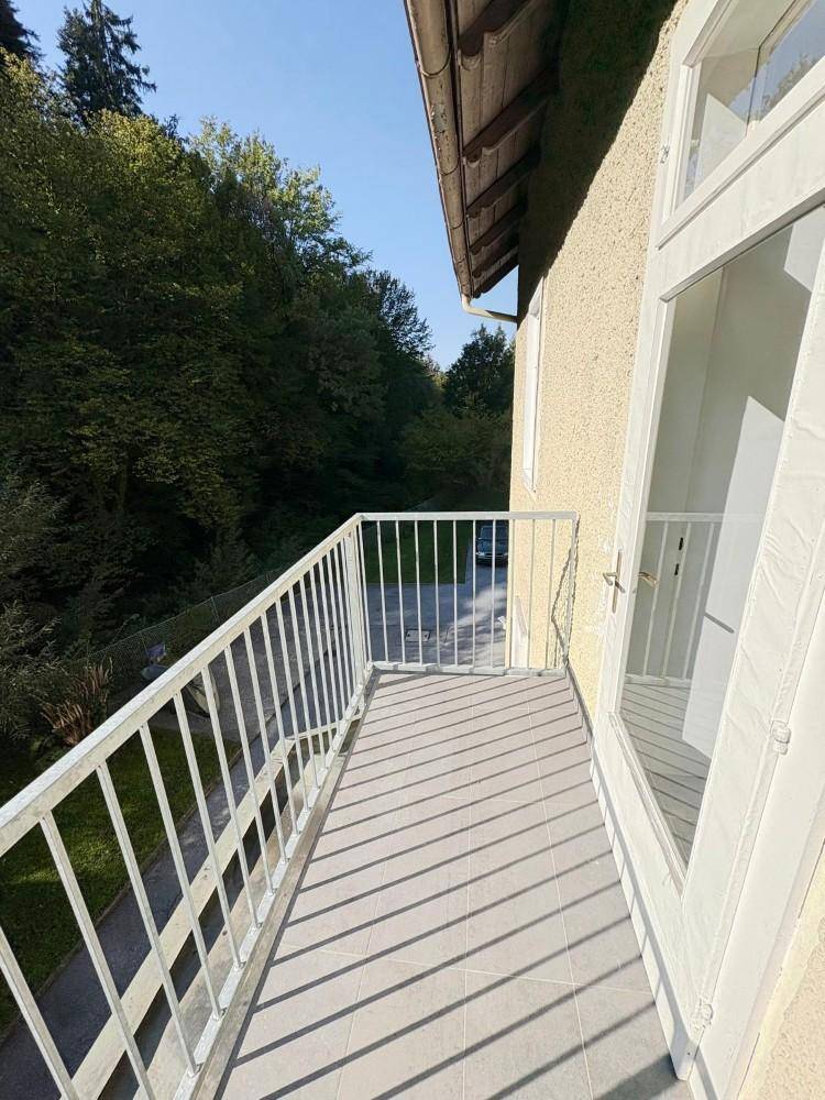 Heller Balkon mit Fliesenboden und weißem Geländer, bietet einen schönen Blick ins Grüne.