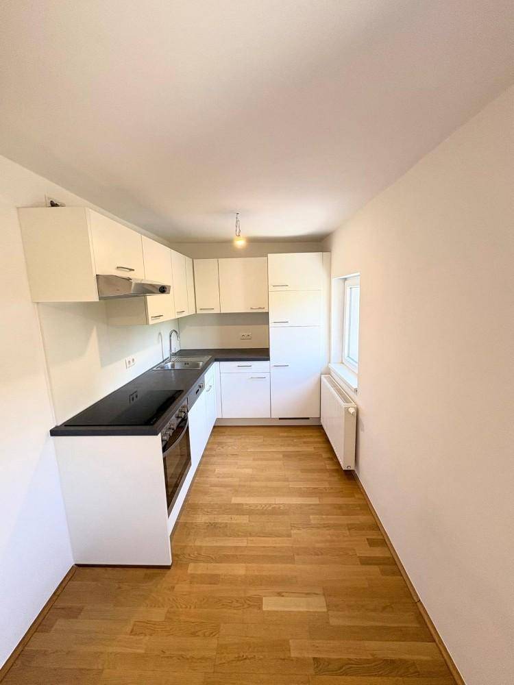 Kompakte Einbauküche in Weiß mit dunkler Arbeitsfläche und Holzfußboden, praktisch und hell.