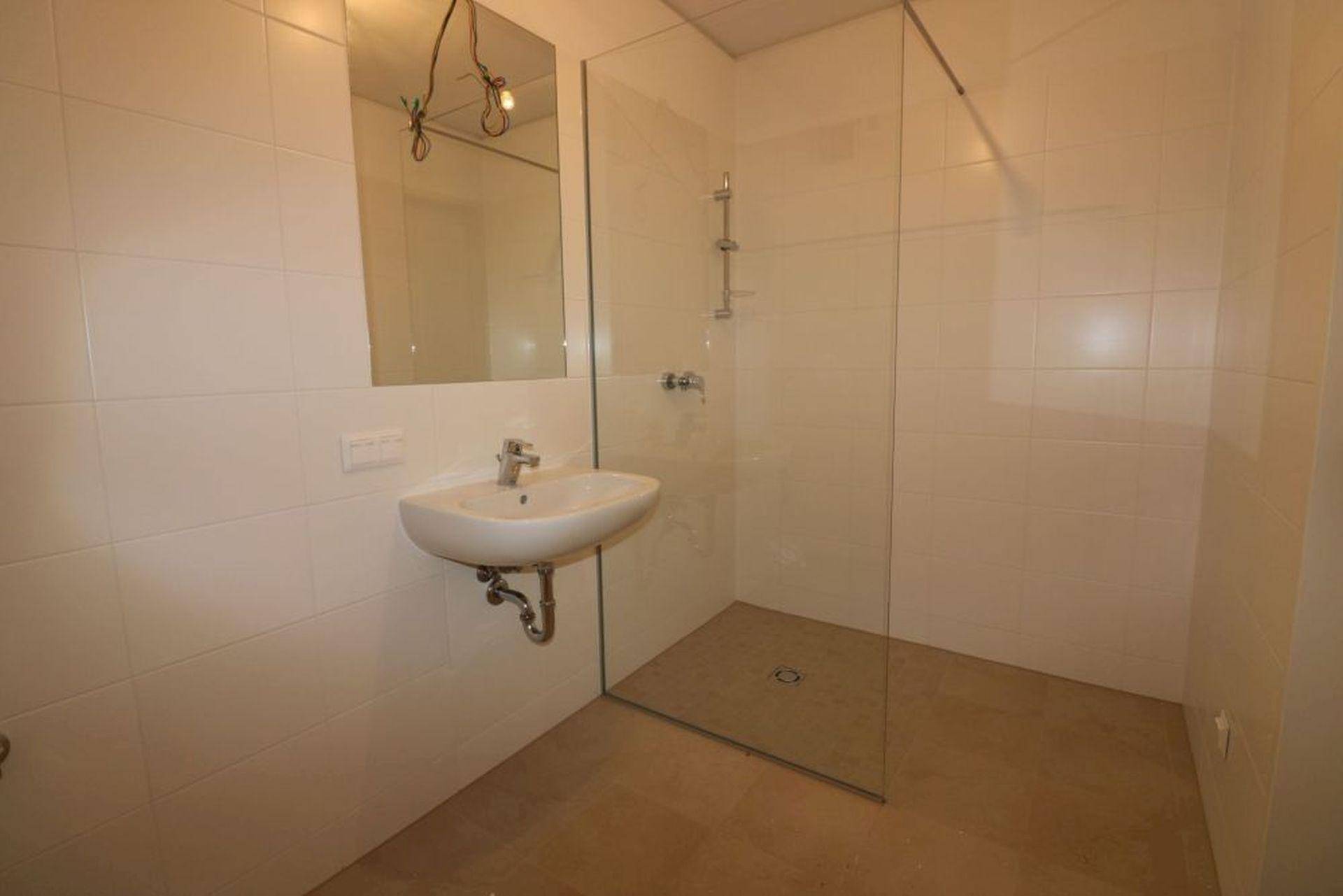Modernes Badezimmer mit weißen Fliesen, ebenerdiger Dusche und Einzelwaschbecken.