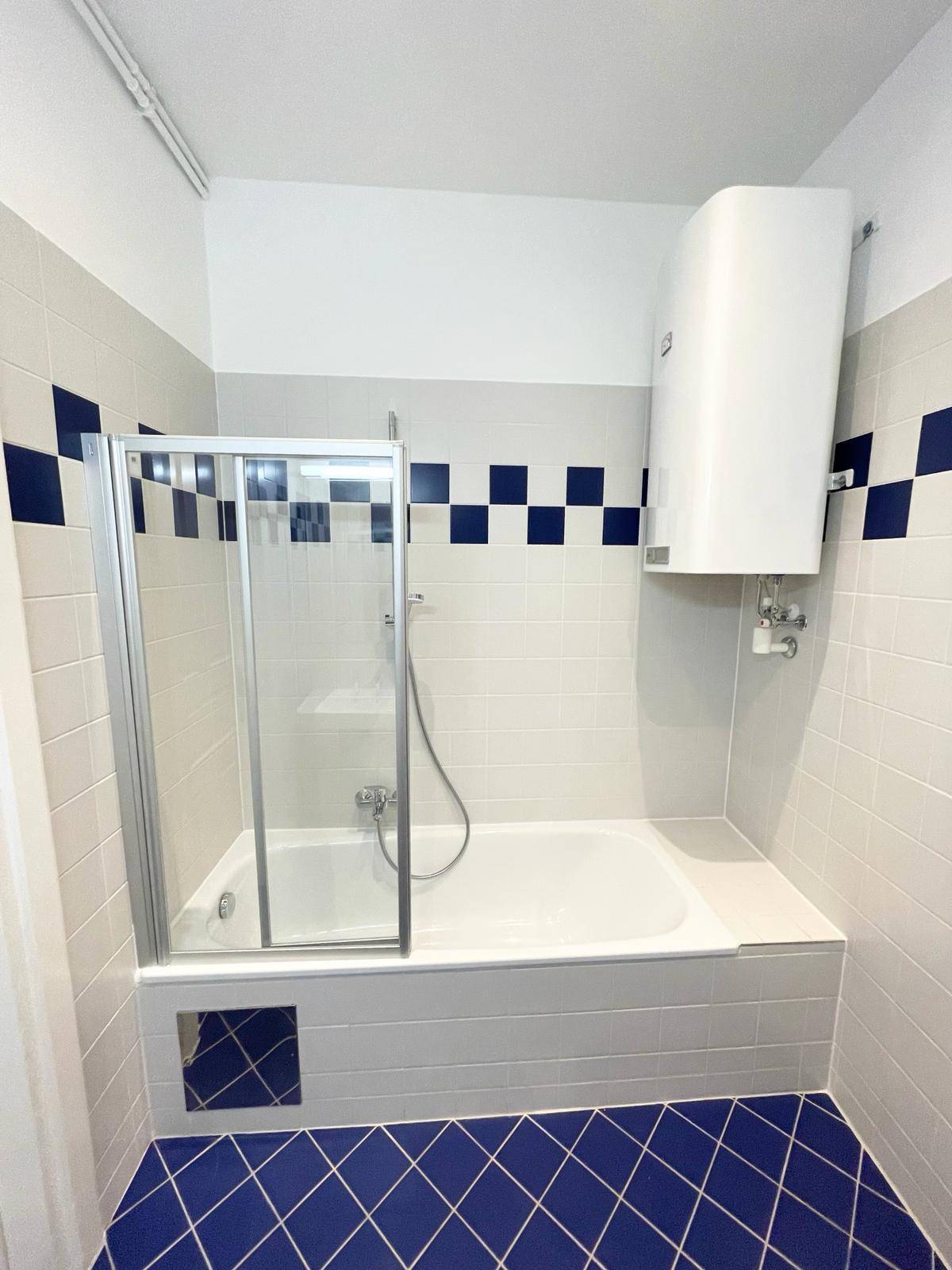 Badezimmer mit Badewanne, Duschabtrennung und blau-weiß karierten Fliesen an den Wänden.