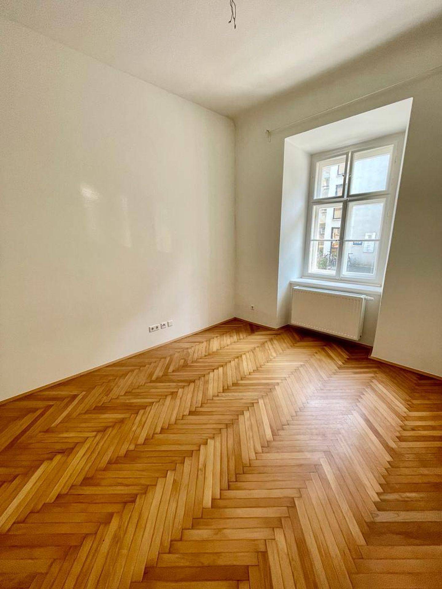 Helles Schlafzimmer mit klassischem Fischgrätparkett und einem großen Fenster.